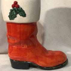 a pair of orange boots with holly decorations on the top and bottom, sitting against a white background