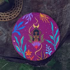 a painted plate sitting on top of a tree stump next to a basket and potted plant