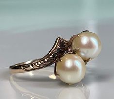 "Pearl ring; Lovely genuine Art Deco pearl engagement ring in 14K rose gold. The two pearls are set in a romantic \"toi et moi\" (you and me) setting. Pearls were often used in engagement and betrothal jewelry at the turn of the century prior to diamonds becoming very popular. The pearls are in beautiful condition and have beautiful lustre. The shoulders of the ring have lovely hand etched detail that is still beautiful and crisp and the prongs are old gothic claw prongs in the Victorian fashion Luxury Rose Gold Pearl Ring Fine Jewelry, Luxury Antique Diamond Pearl Ring, Luxury Timeless Pearl Ring With Prong Setting, Luxury Vintage Pearl Ring For Formal Events, Luxury Classic White Pearl Ring, Luxury Yellow Gold Pearl Drop Ring, Luxury Elegant Pearl Ring With Halo Design, Luxury Pearl Ring With Rose Cut Diamonds For Wedding, Luxury Intricate Design Pearl Ring For Anniversary