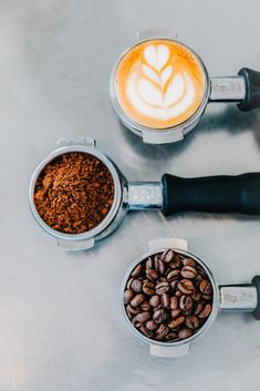 three coffee mugs filled with different types of coffee beans on top of a table