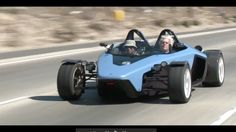 a man driving a blue race car down a road with two people in the back