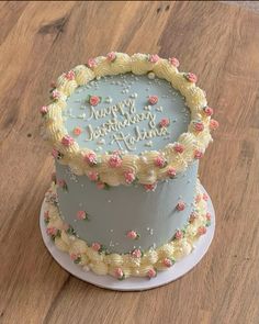 a birthday cake with frosting and flowers on it sitting on a table next to a wooden floor