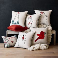 four pillows with red and white designs are on a bench in front of a black wall