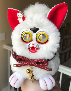 a white stuffed animal with yellow eyes and red bow tie on it's head