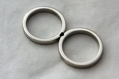 two silver rings sitting on top of a white sheet with black dots in the middle