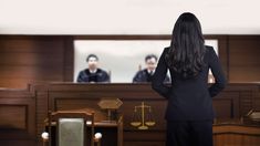 a woman standing in front of a courtroom with her back to the camera, looking at two men