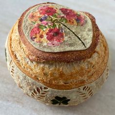 a round piece of bread with flowers painted on the top and bottom, sitting on a white surface