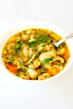 a white bowl filled with chicken and vegetable soup on top of a table next to a spoon