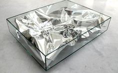 a glass coffee table with silver foil covering the top and bottom part, on concrete flooring