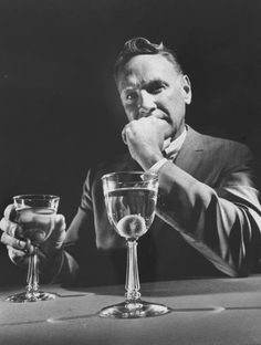 a man sitting at a table with two wine glasses in front of him and his chin resting on his hand