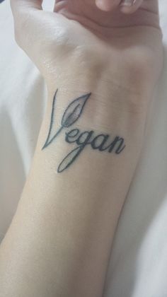 a woman with a tattoo on her arm that says vegan in cursive writing