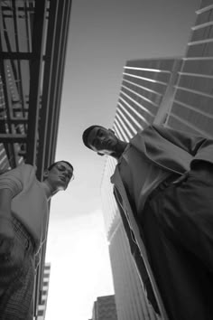 two men standing next to each other in front of tall buildings with skyscrapers behind them