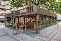 an outdoor restaurant with wooden tables and chairs on the side walk in front of a building