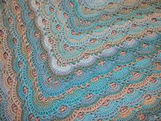 a crocheted blanket is laying on top of a bed with blue and green colors