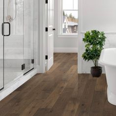 a bathroom with white walls and wood flooring next to a bathtub in the corner