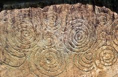 an intricately carved rock with circles and spirals on it's sides, in the desert