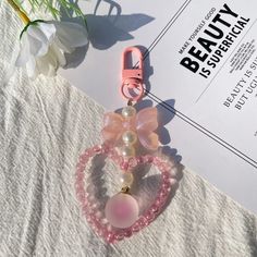 a pink heart shaped keychain sitting on top of a white sheet next to a flower