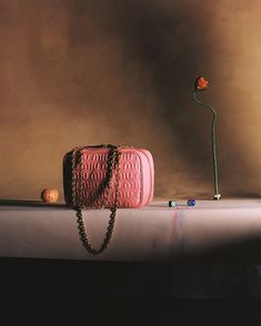 a pink handbag sitting on top of a table next to a small orange flower