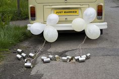 balloons tied to the back of a yellow car with just married written on it in white