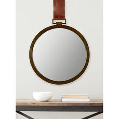 a round mirror sitting on top of a wooden table next to a white bowl and book