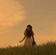 a woman in a dress standing on top of a lush green field under a cloudy sky