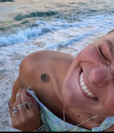 a woman smiles as she lays on the beach next to the ocean with her eyes closed