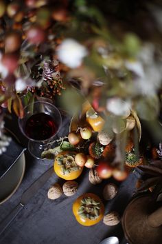 an arrangement of fruit, nuts and wine on a table with other items in the background