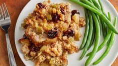 a white plate topped with green beans and stuffing next to a fork on a wooden table