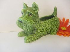 a green ceramic dog planter sitting next to an orange flower