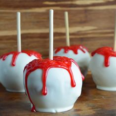 white chocolate covered apples with red drizzled on them sitting on a wooden table