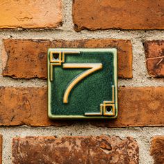 a brick wall with a green and gold house number seven on it's side