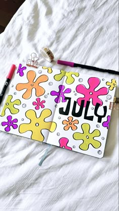 an open notebook with the word july written on it next to a marker and pencil