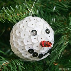 a white ornament hanging from a christmas tree with black and red buttons on it