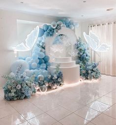 a white and blue wedding cake surrounded by balloons, flowers, and lights in a room