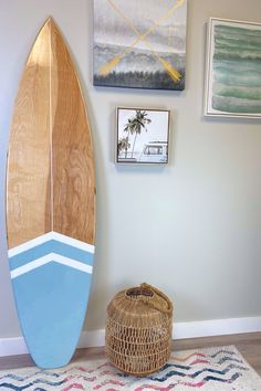 a surfboard leaning up against the wall next to a basket and pictures on the wall