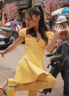 a woman in a yellow dress is dancing on the street