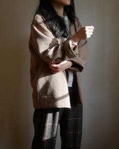 a woman standing in front of a wall with her arms crossed and looking off to the side