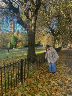 a woman walking down a leaf covered sidewalk next to a tree filled with lots of leaves