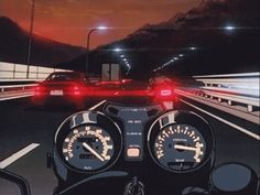 a motorcycle driving down a highway next to a red light at night with the lights on