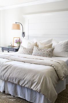 a bed with white linens and pillows in a small room next to a lamp