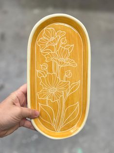 a person holding up a wooden tray with flowers on it and the lid painted yellow