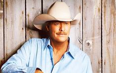 a man wearing a cowboy hat leaning against a wooden wall with his arms crossed and looking at the camera