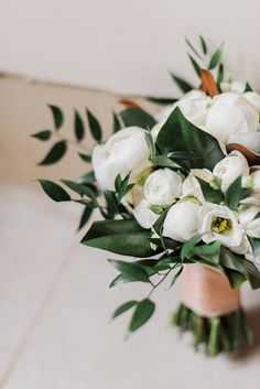 a bridal bouquet with white flowers and greenery on the side of a wall