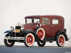 an old model car is parked in front of a white wall with red rims