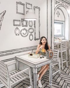 a woman sitting at a table in front of a drawing on the wall behind her