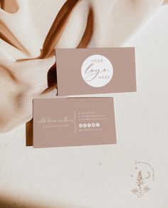 two business cards sitting on top of a white cloth covered tablecloth with a logo