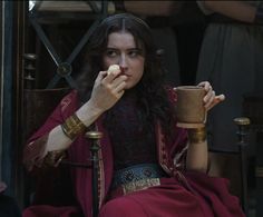 a woman sitting down holding a cup in her hand and eating something out of it