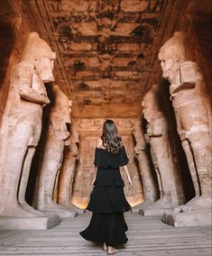 a woman in a black dress walking through an egyptian temple