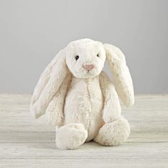 a white stuffed rabbit sitting on top of a wooden table next to a gray wall