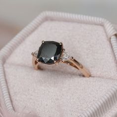 a black diamond ring sitting on top of a white cloth covered cushioned box with its lid open